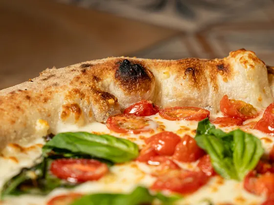 Il cornicione di una pizza con pomodorini e basilico, in primo piano