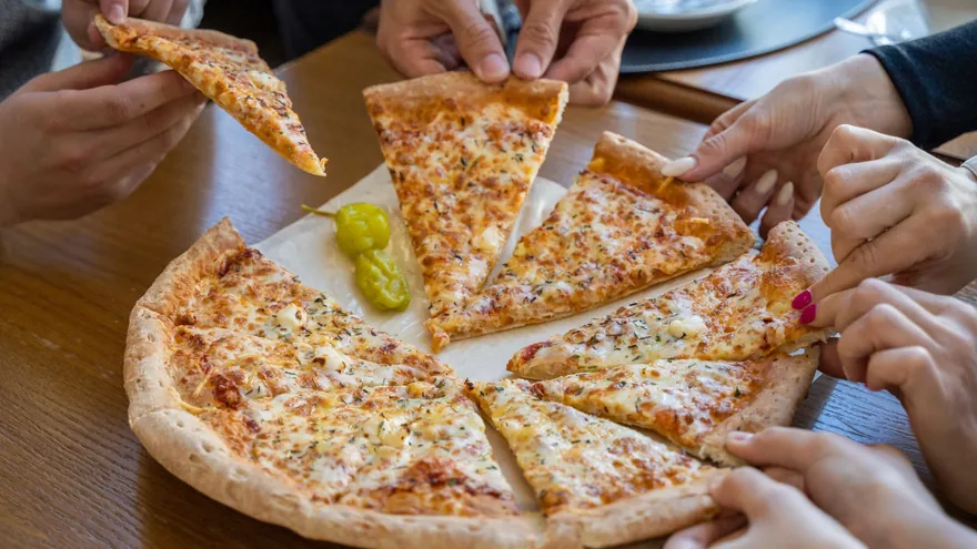 Mani che prendono le fette da una pizza al centro del tavolo