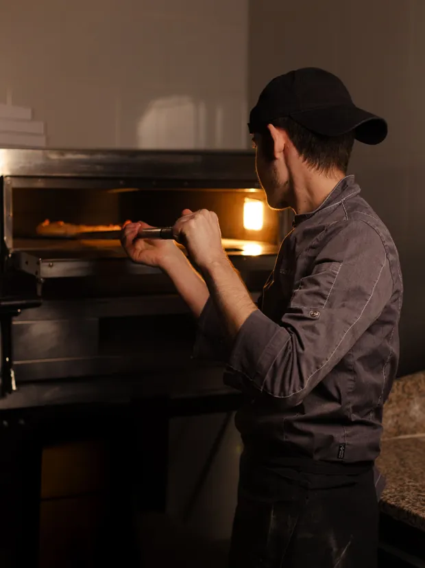 Un pizzaiolo infila la pala dentro il forno