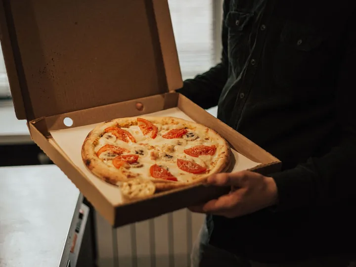 Una pizza dentro la scatola d'asporto aperta, tenuta fra le mani