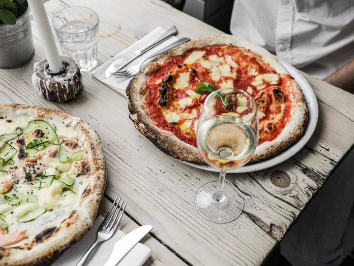 Due pizze servite su un tavolo apparecchiato, con bicchieri e posate